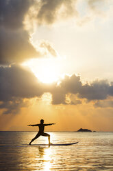 Thailand, man doing yoga on paddleboard at sunset, bridge position, warrior pose - SBOF000178