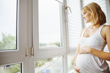 Pregnant woman holding her belly, looking through window - ZEDF000288