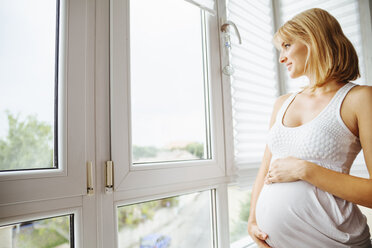 Schwangere Frau hält ihren Bauch und schaut durch ein Fenster - ZEDF000288