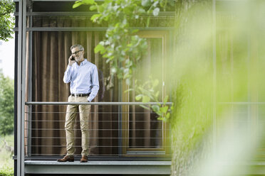 Mann am Telefon auf dem Balkon seines Hauses stehend - SBOF000189