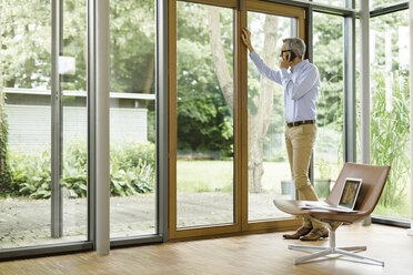 Man on the phone standing in his living room looking through window - SBOF000226