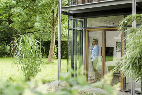 Mann telefoniert in seinem Haus und schaut durch ein Fenster, lizenzfreies Stockfoto