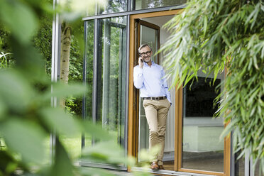 Man on the phone standing at open door of his house - SBOF000232