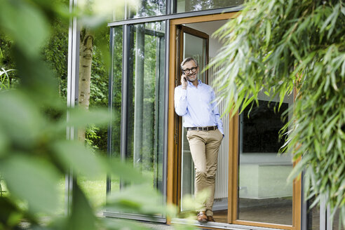 Mann am Telefon vor der offenen Tür seines Hauses - SBOF000232