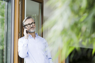 Man on the phone standing at open door of his house - SBOF000233