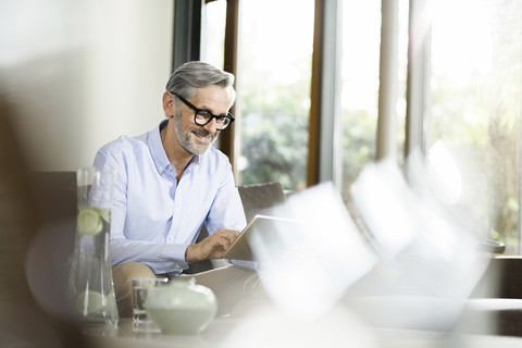 Mann sitzt im Wohnzimmer und benutzt ein Tablet, lizenzfreies Stockfoto