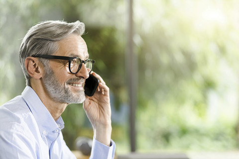 Lächelnder Mann mit grauem Haar und Bart am Telefon, lizenzfreies Stockfoto
