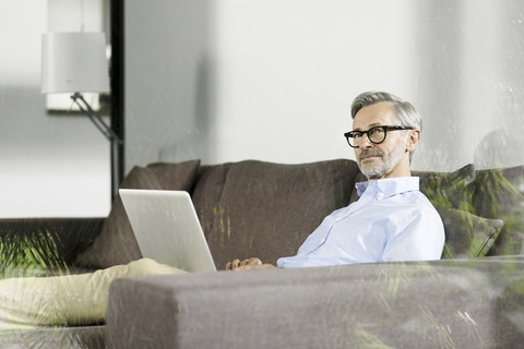 Mann sitzt auf der Couch in seinem Wohnzimmer mit Laptop, lizenzfreies Stockfoto