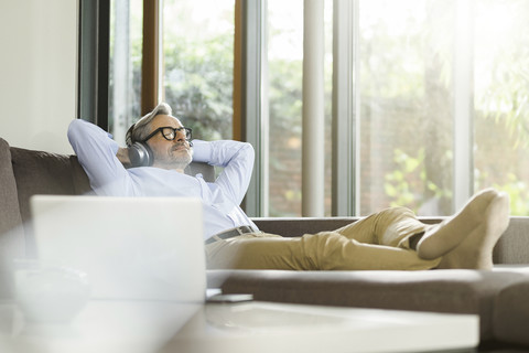 Man relaxing on the couch listening music with headphones stock photo