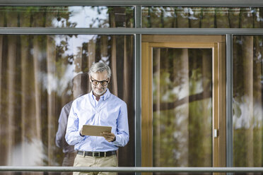 Mann steht auf dem Balkon seines Hauses und schaut auf ein Tablet - SBOF000247