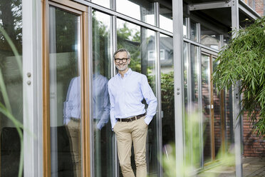 Smiling man leaning against facade of his house - SBOF000253