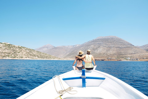 Greece, back view of couple sitting arm in arm on bow of a boat looking at Amorgos Island stock photo