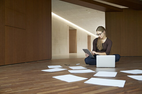 Junge Frau sitzt auf dem Boden und arbeitet mit Tablet und Laptop - FMKF003084