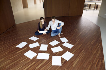 Young woman and young man sitting on floor working together - FMKF003085