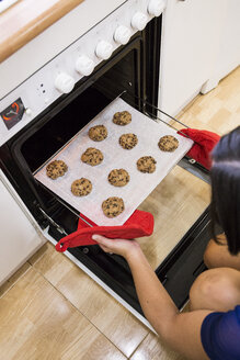 Frau nimmt frisch gebackene Kekse aus dem Ofen - ABZF001058