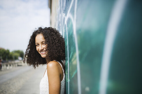 Portrait of smiling young woman leaning against wall - MRAF000133