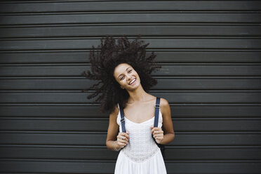 Portrait of smiling young woman standing in front of roller shutter shaking her head - MRAF000135