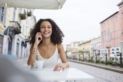 Porträt einer lächelnden jungen Frau, die in einem Straßencafé telefoniert, lizenzfreies Stockfoto