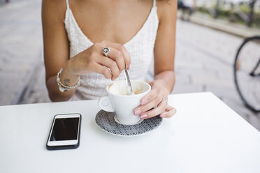 Die Hand einer jungen Frau rührt in einem Straßencafé Cappuccino um - MRAF000141