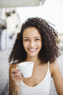 Porträt einer glücklichen jungen Frau, die in einem Straßencafé Kaffee trinkt - MRAF000144