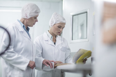 Zwei Labortechniker in steriler Schutzkleidung sehen sich Akten an - ZEF010025