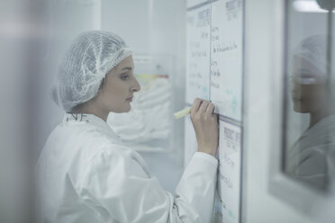 Labortechniker in steriler Schutzkleidung schreibt Notizen auf einer Tafel - ZEF010027