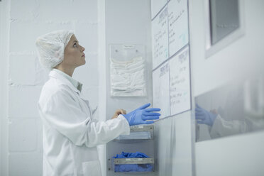 Lab technician putting on latex gloves looking on whiteboard - ZEF010029