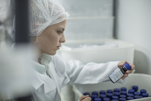 Lab worker in pharmaceutical plant looking at pill bottle - ZEF010039