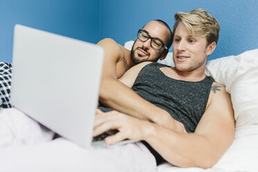 Schwules Paar im Bett liegend, mit Laptop - MADF001137