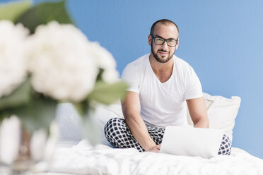 Gay man sitting on bed, using laptop - MADF001145