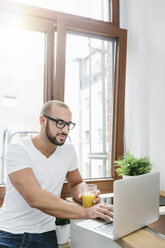 Gay man drinking orange juice while reading emails - MADF001168