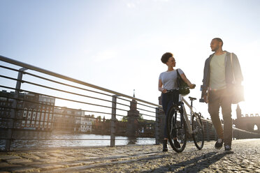 Couple walking by river, pushing bicycle - FKF002053
