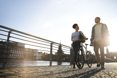 Paar, das am Fluss spazieren geht und ein Fahrrad schiebt - FKF002053