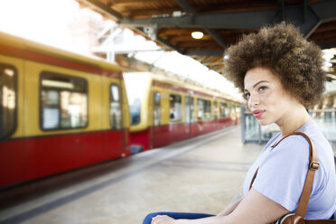 Junge Frau sitzt auf einer Bank am Bahnhof - FK002058