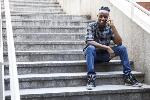 Junger Mann sitzt auf einer Treppe und benutzt ein Smartphone - ABZF001106