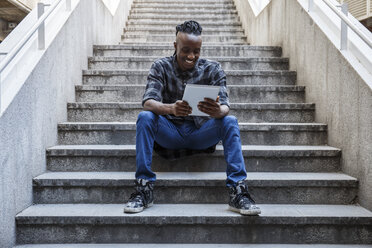 Young man sitting on stairs, using digital tablet - ABZF001110