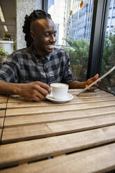 Young man sitting in cafe, using digital tablet - ABZF001121