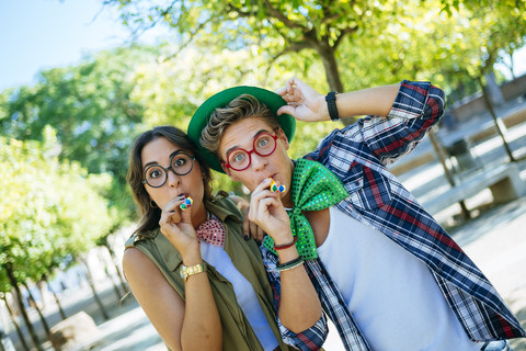 Junges Paar hat Spaß mit Partybläsern, Scherzbrillen und Mützen, lizenzfreies Stockfoto