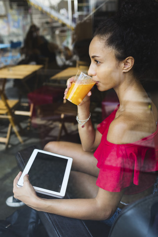 Junge Frau trinkt ein Glas Orangensaft in einem Café, lizenzfreies Stockfoto