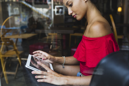 Junge Frau sitzt in einem Café und benutzt ein Tablet - MRAF000154