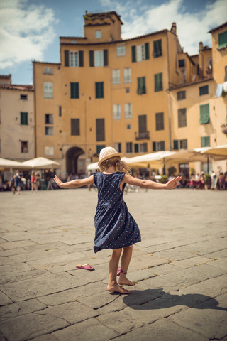 Italien, Lucca, Rückansicht eines tanzenden kleinen Mädchens auf der Piazza dell'Anfiteatro, lizenzfreies Stockfoto