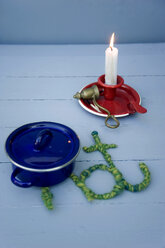 Blue cooking pot on table mat made from wool and wire with burning candle in background - GISF000246