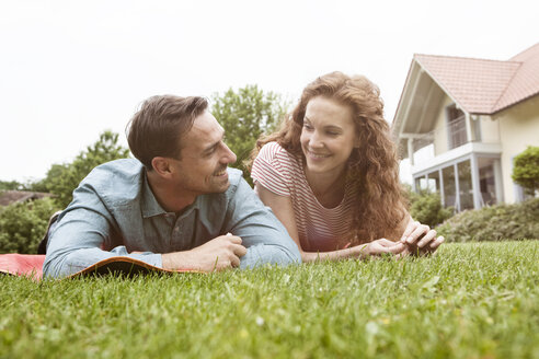 Lächelndes Paar auf dem Rasen im Garten liegend - RBF005079