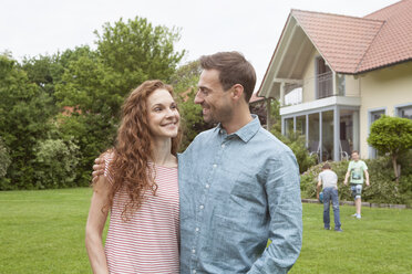 Lächelndes Paar im Garten mit Kindern im Hintergrund - RBF005081