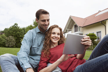 Lächelndes Paar sitzt im Garten und benutzt ein Tablet - RBF005083