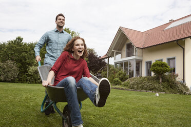 Man pushing happy woman in wheelbarrow in garden - RBF005091