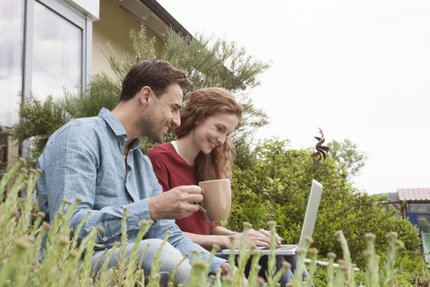 Smiling couple sitting in garden using laptop stock photo