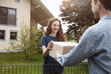 Frau am Gartenzaun nimmt Paket entgegen - RBF005097