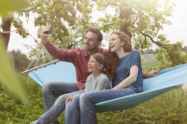 Happy family sitting in hammmock taking a selfie - RBF005106