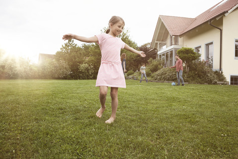 Mädchen tanzt im Garten mit Familie im Hintergrund, lizenzfreies Stockfoto